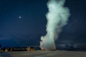 Old Faithful geyser on a winter night with stars