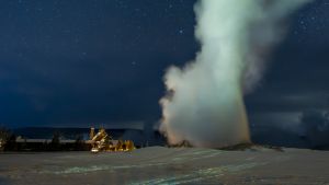 Old Faithful Geyser with snow and stars at night.