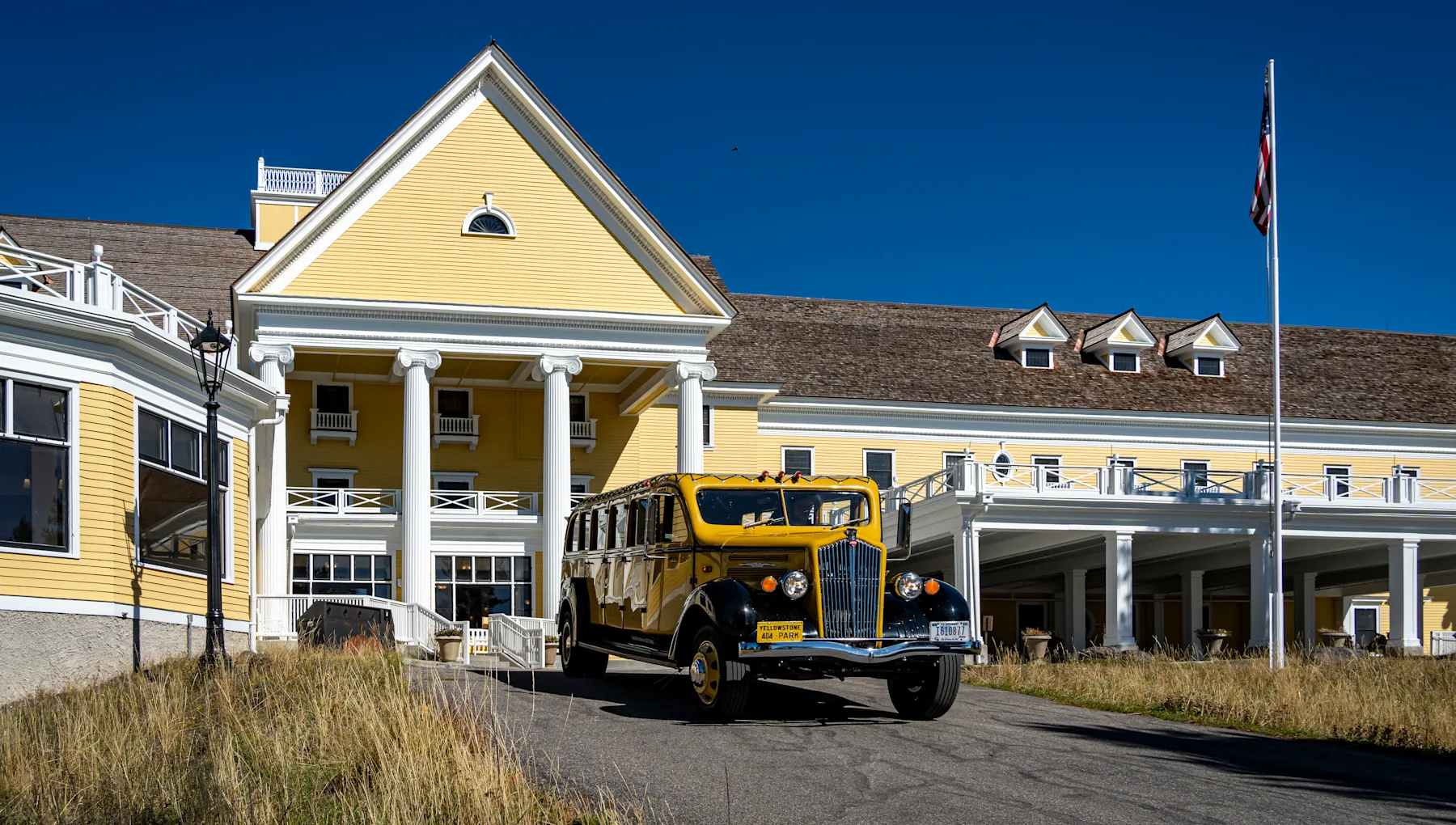 Entrance to Lake Yellowstone Hotel with a historic yellow bus in the driveway