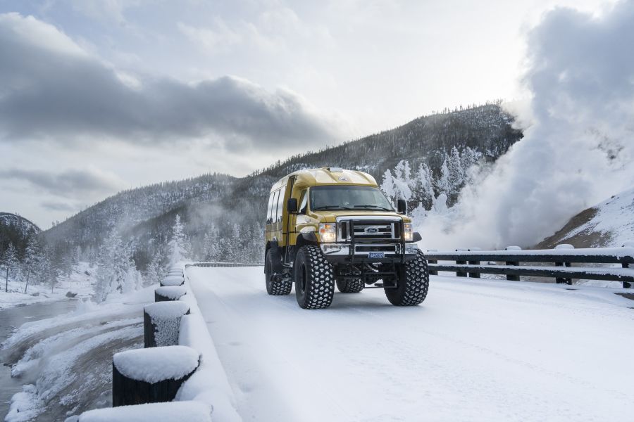 Snowcoach crossing snow-covered bridge with fumarole