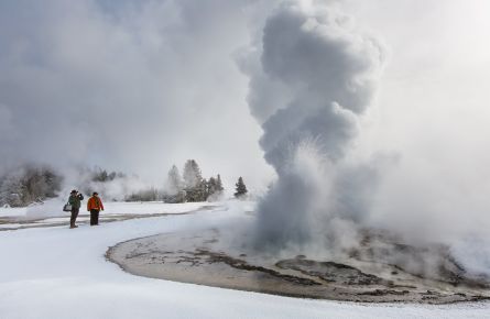 Two people watching a geyser in the snow