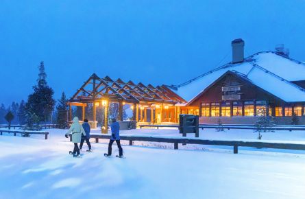 Old Faithful Snow Lodge exterior in winter with people snowshoeing in front